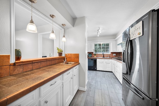 kitchen with hanging light fixtures, stainless steel fridge, white cabinetry, and sink