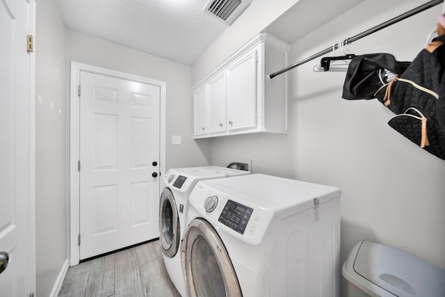 laundry area with cabinets, a textured ceiling, light hardwood / wood-style floors, and washer and dryer