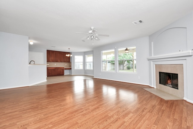 unfurnished living room with a tile fireplace, ceiling fan with notable chandelier, and light hardwood / wood-style flooring