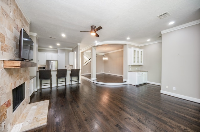 unfurnished living room with dark wood-type flooring, a stone fireplace, a textured ceiling, crown molding, and ceiling fan