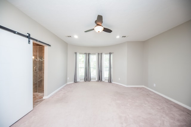 empty room featuring ceiling fan, carpet flooring, and a barn door