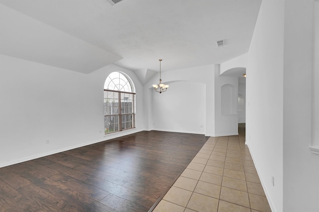 empty room featuring a notable chandelier, wood-type flooring, and vaulted ceiling