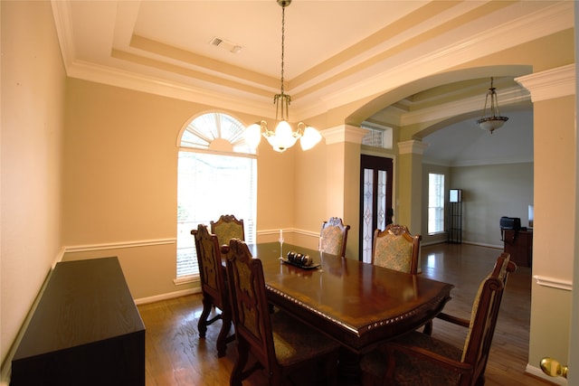 dining space featuring crown molding, a tray ceiling, decorative columns, dark hardwood / wood-style floors, and a chandelier