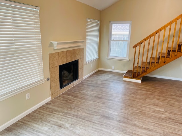 unfurnished living room with lofted ceiling, light hardwood / wood-style flooring, and a tile fireplace