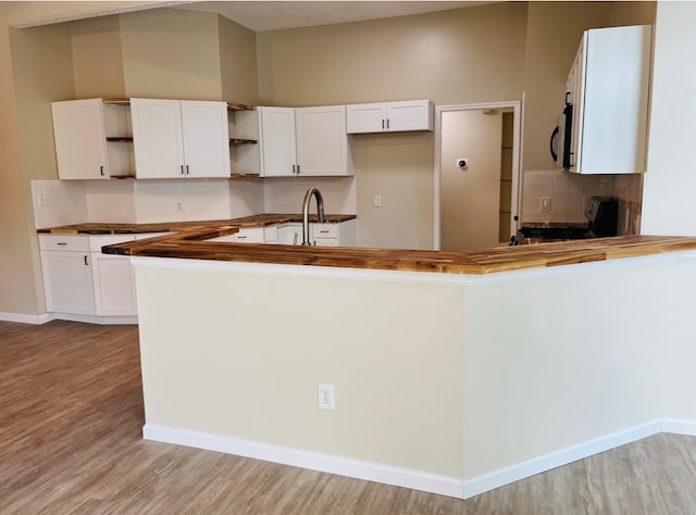 kitchen with kitchen peninsula, light hardwood / wood-style flooring, range, white cabinetry, and decorative backsplash