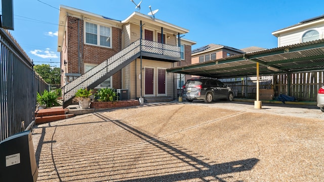 back of house featuring a balcony, central AC unit, and a carport