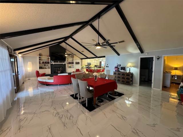 dining room featuring ceiling fan, a fireplace, lofted ceiling with beams, and a textured ceiling