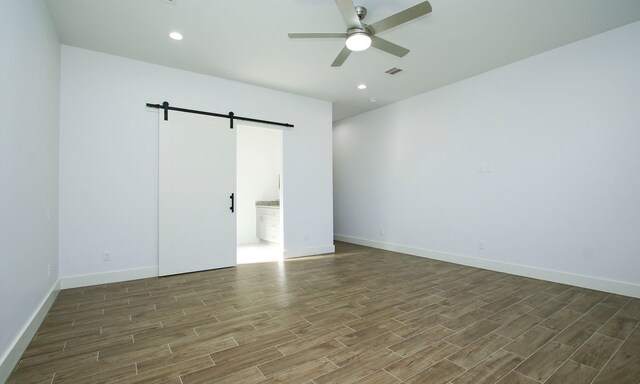 unfurnished room featuring a barn door, ceiling fan, and dark hardwood / wood-style flooring