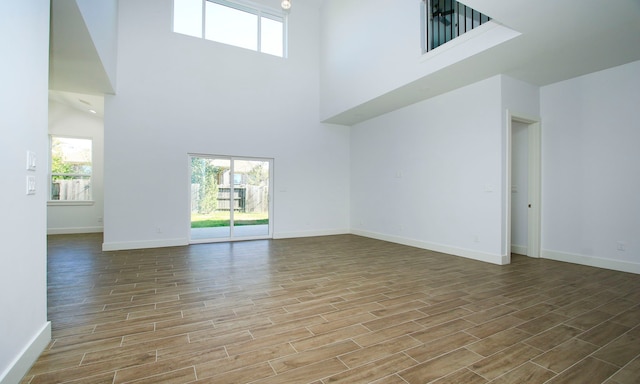 unfurnished living room featuring a towering ceiling, a healthy amount of sunlight, and hardwood / wood-style flooring