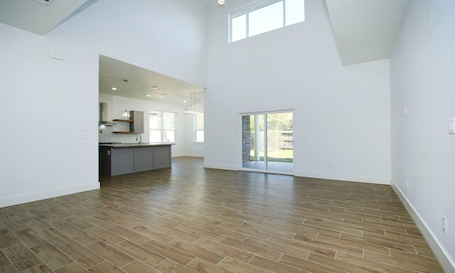 unfurnished living room with wood-type flooring, sink, and a towering ceiling