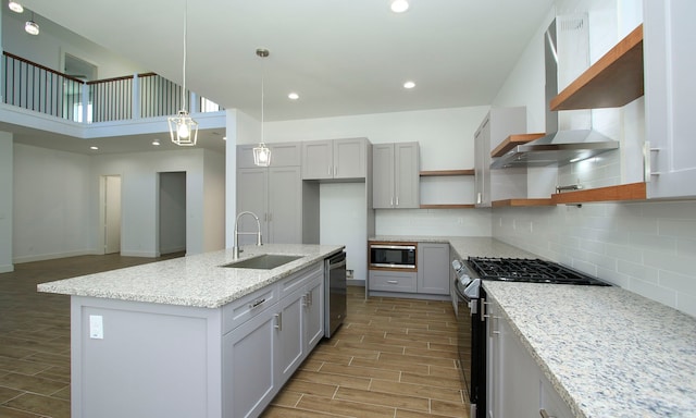 kitchen with light stone countertops, stainless steel appliances, wall chimney range hood, decorative light fixtures, and hardwood / wood-style flooring