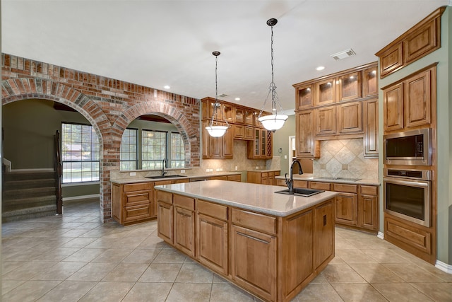 kitchen featuring decorative light fixtures, a center island with sink, sink, stainless steel appliances, and light tile patterned floors