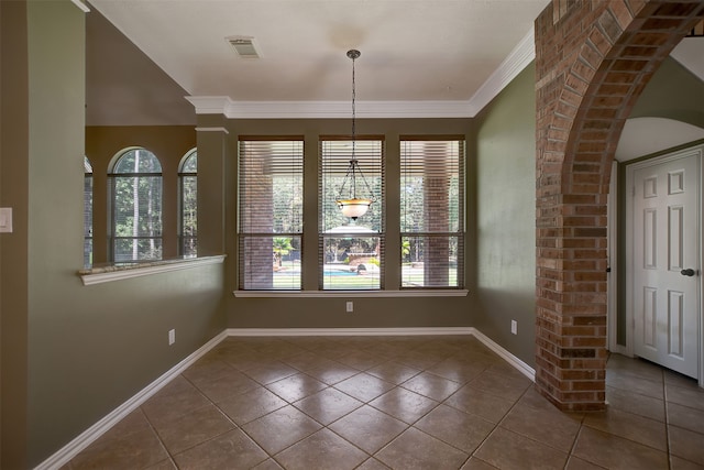 unfurnished dining area featuring tile patterned flooring, ornate columns, crown molding, and a wealth of natural light