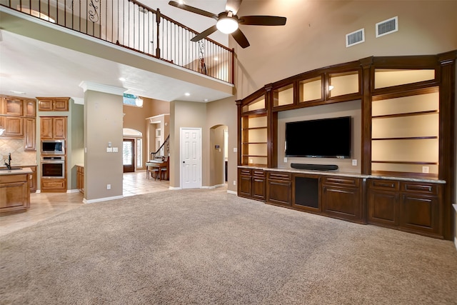 unfurnished living room featuring ceiling fan, light colored carpet, a towering ceiling, sink, and ornamental molding