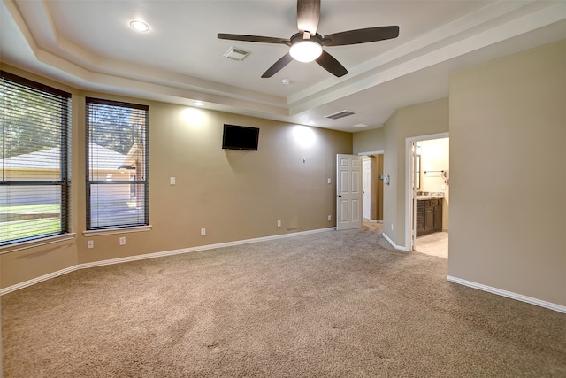 spare room with a tray ceiling, light colored carpet, and ceiling fan