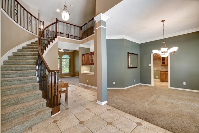 carpeted entrance foyer with ornate columns, crown molding, a towering ceiling, and ceiling fan with notable chandelier