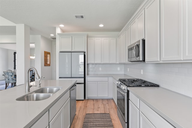 kitchen with stainless steel appliances, sink, light wood-type flooring, white cabinetry, and tasteful backsplash