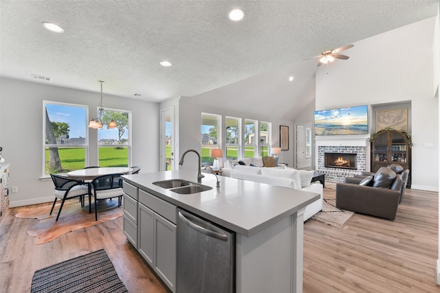 kitchen with stainless steel dishwasher, a kitchen island with sink, a fireplace, and light wood-type flooring