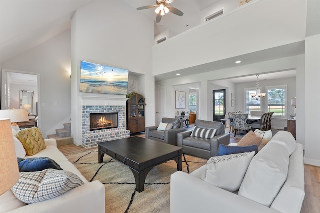 living room featuring light hardwood / wood-style flooring, high vaulted ceiling, ceiling fan with notable chandelier, and a brick fireplace