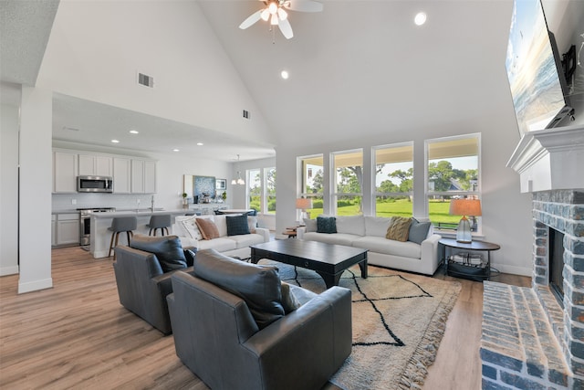 living room with light hardwood / wood-style floors, high vaulted ceiling, a brick fireplace, and ceiling fan