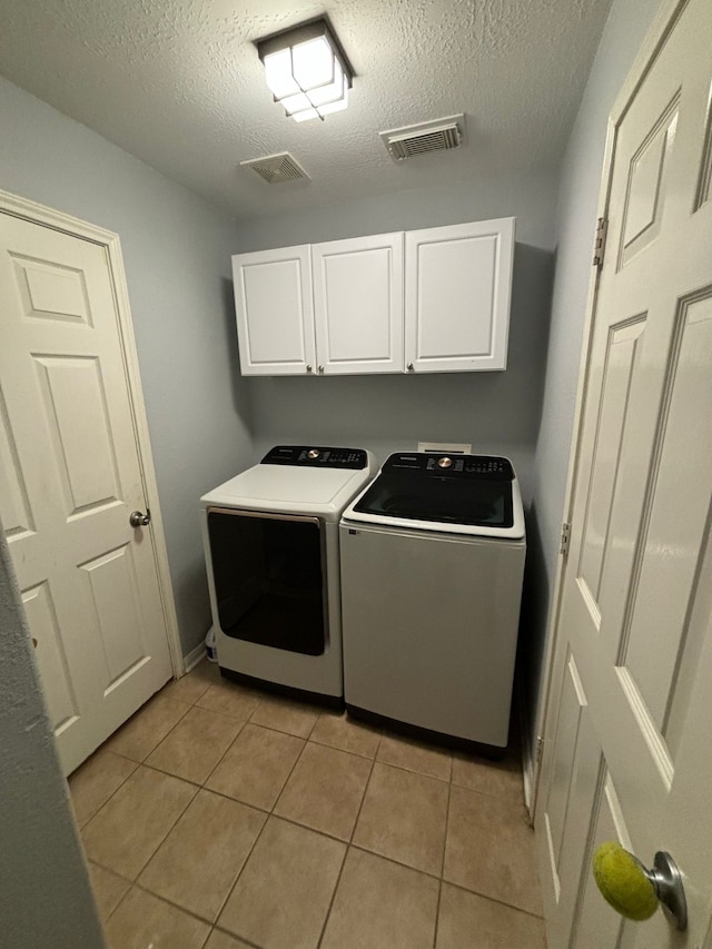 laundry area with a textured ceiling, separate washer and dryer, light tile patterned floors, and cabinets