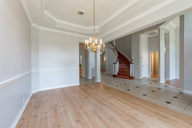 empty room with a notable chandelier, ornamental molding, a tray ceiling, and light wood-type flooring