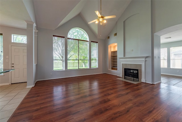 unfurnished living room with hardwood / wood-style floors, high vaulted ceiling, a tile fireplace, and a wealth of natural light