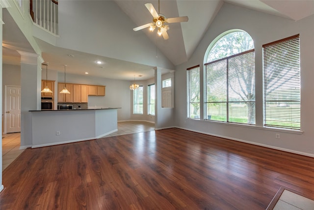 unfurnished living room featuring wood-type flooring, ornate columns, high vaulted ceiling, and a healthy amount of sunlight