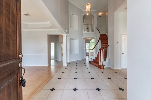 entryway with a towering ceiling, crown molding, ornate columns, and light hardwood / wood-style floors