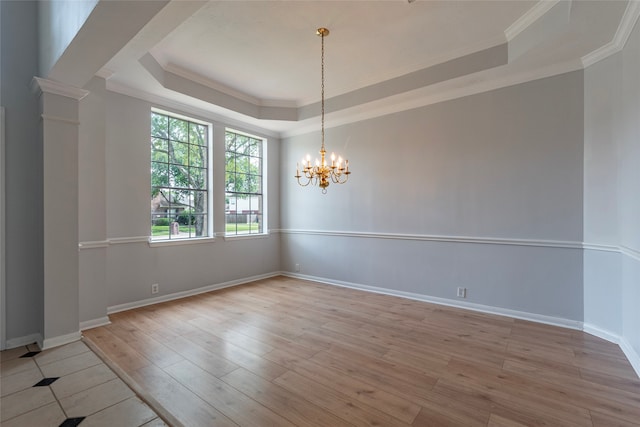 spare room featuring a raised ceiling, an inviting chandelier, decorative columns, light hardwood / wood-style floors, and crown molding