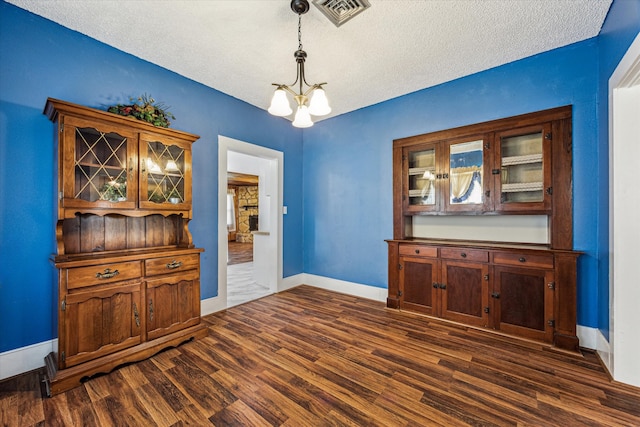 unfurnished dining area with a textured ceiling, dark hardwood / wood-style flooring, and a notable chandelier