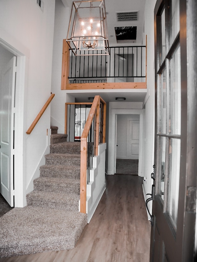 staircase featuring hardwood / wood-style floors, a towering ceiling, and an inviting chandelier