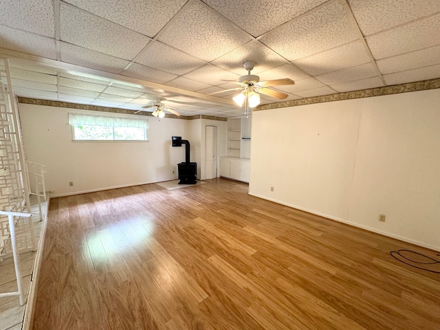 unfurnished living room featuring a drop ceiling, a wood stove, ceiling fan, and hardwood / wood-style floors