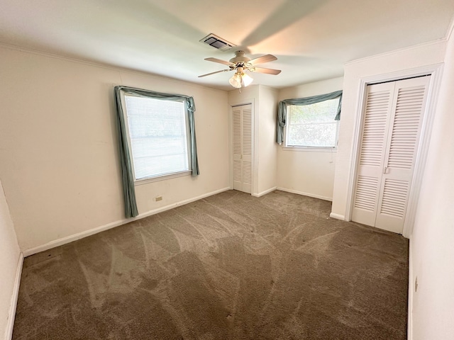 unfurnished bedroom with dark carpet, multiple closets, and ceiling fan