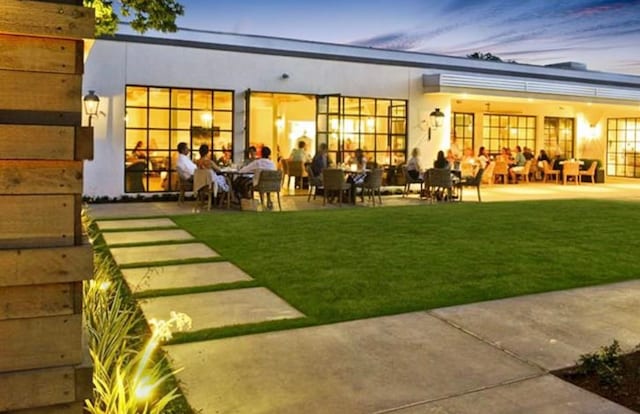 back house at dusk featuring a lawn and a patio area