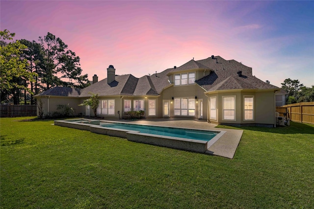 back house at dusk with a lawn, a patio area, and a fenced in pool