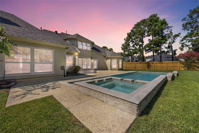 pool at dusk with an in ground hot tub, a patio area, and a lawn