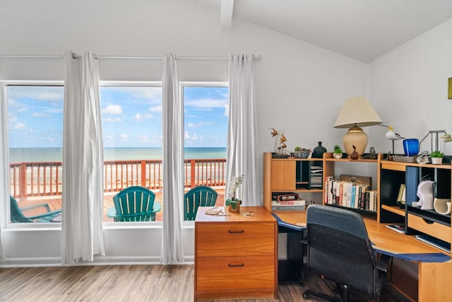 office space with a water view, a view of the beach, light hardwood / wood-style flooring, and vaulted ceiling with beams