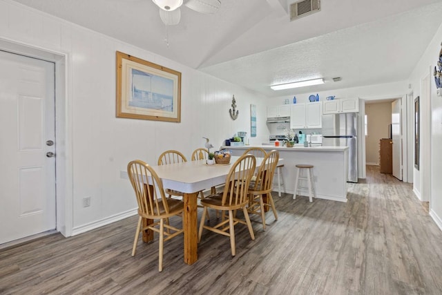 dining room with a textured ceiling, vaulted ceiling, wood-type flooring, and ceiling fan