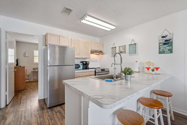 kitchen with light brown cabinets, dark hardwood / wood-style floors, a kitchen breakfast bar, kitchen peninsula, and stainless steel appliances