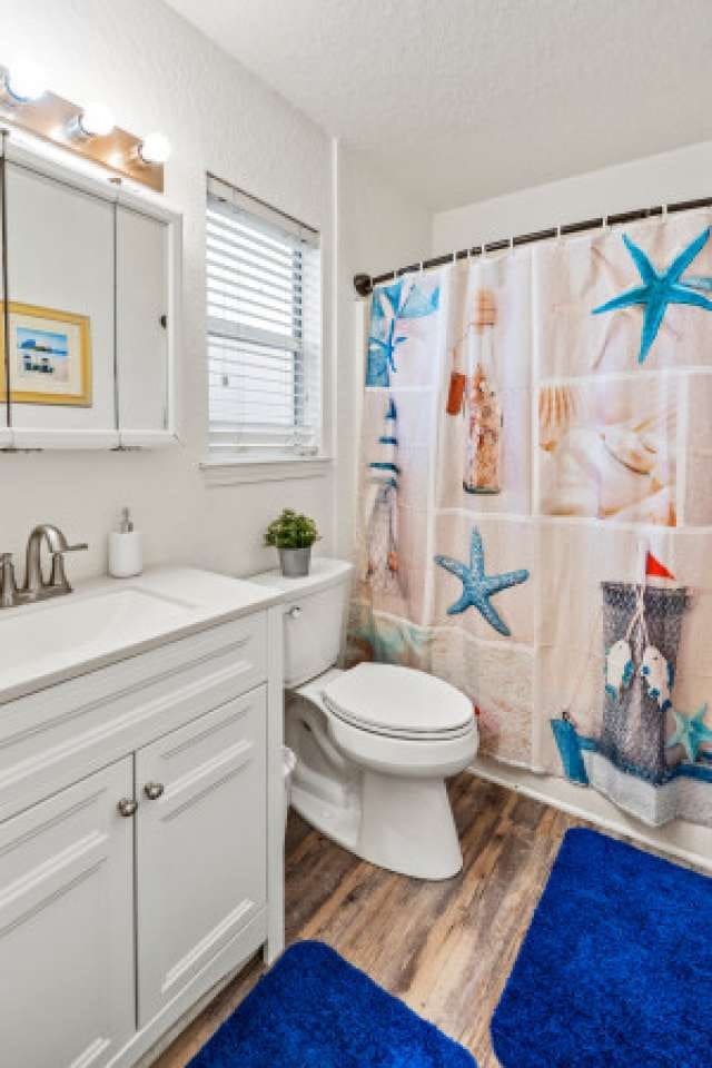 bathroom featuring a textured ceiling, wood-type flooring, toilet, vanity, and curtained shower