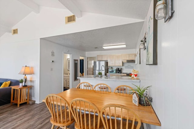 dining room with vaulted ceiling with beams, a textured ceiling, and hardwood / wood-style flooring