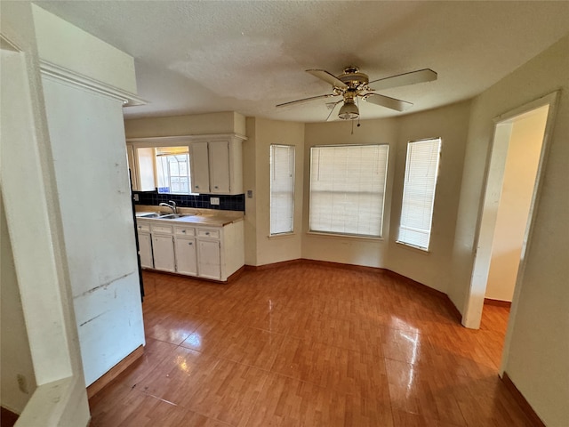 kitchen with light wood-type flooring, sink, white cabinets, decorative backsplash, and ceiling fan