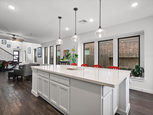 kitchen featuring white cabinetry, ceiling fan, hanging light fixtures, a center island, and dark hardwood / wood-style flooring