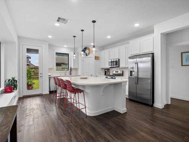 kitchen featuring dark wood-type flooring, white cabinets, hanging light fixtures, tasteful backsplash, and appliances with stainless steel finishes