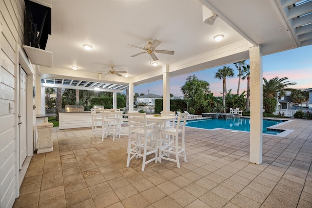 pool at dusk featuring a patio, ceiling fan, and exterior kitchen