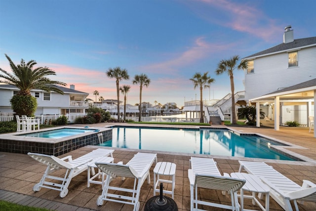 pool at dusk featuring a patio area and an in ground hot tub