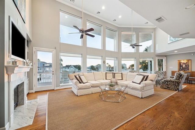 living room with a towering ceiling, ornamental molding, a high end fireplace, ceiling fan, and light wood-type flooring