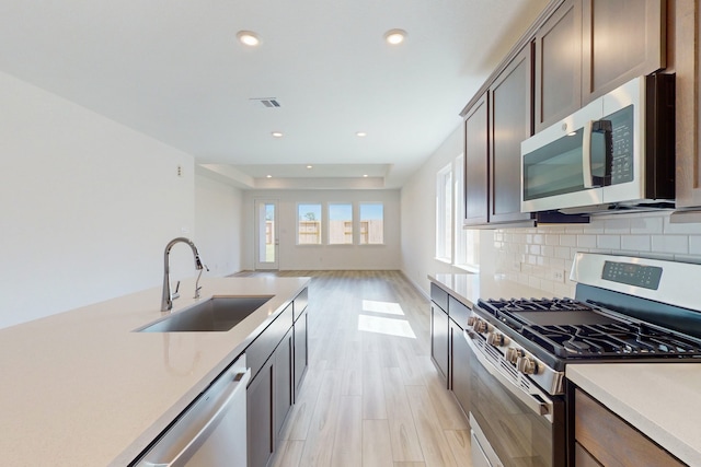 kitchen with dark brown cabinetry, sink, tasteful backsplash, stainless steel appliances, and light hardwood / wood-style floors