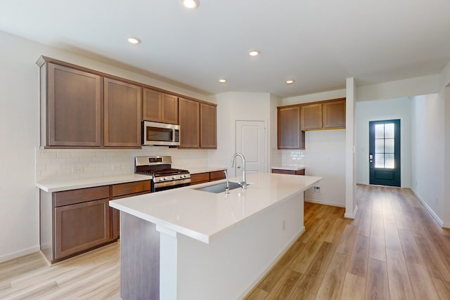 kitchen with light hardwood / wood-style floors, sink, decorative backsplash, stainless steel appliances, and a center island with sink